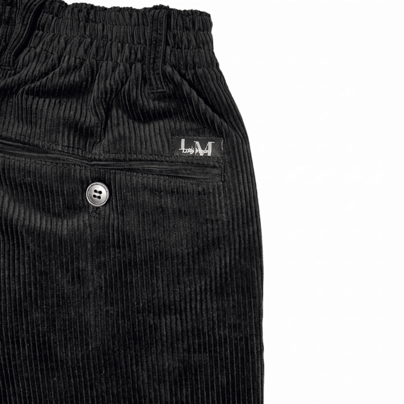 Gros plan sur le tissu en velours côtelé noir, une poche arrière boutonnée et la taille élastique du pantalon
