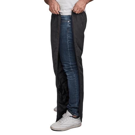 Man ritst zwarte Dobsom thermobroek open aan de zijkant, over blauwe jeans en witte sneakers