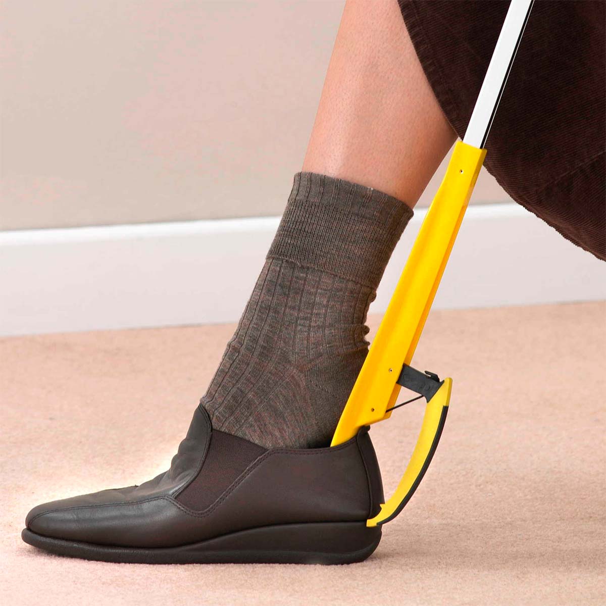 Une personne utilise la pince de préhension jaune comme chausse-pied pour enfiler une chaussure marron foncé